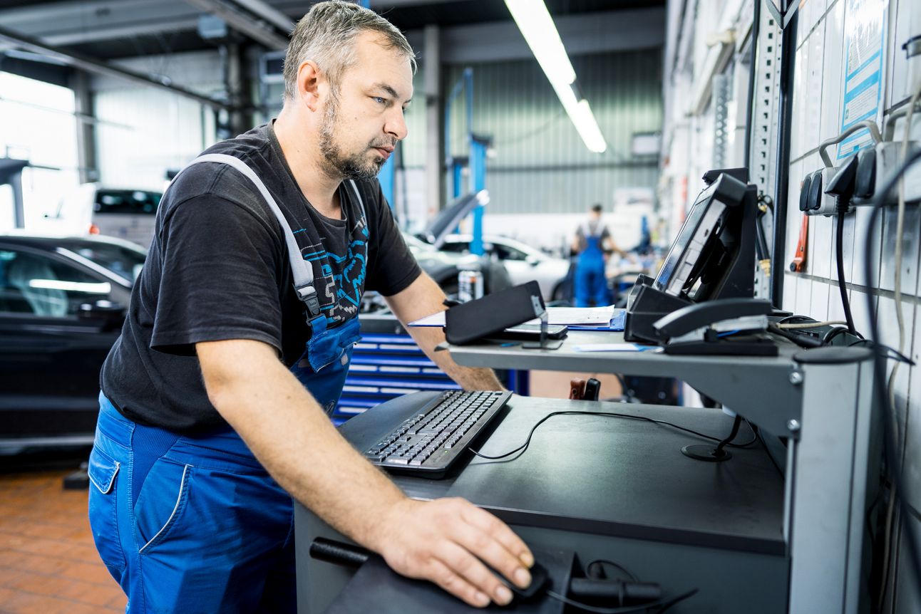 Kfz-Mechatroniker in Werkstatt steht vor Pult mit PC