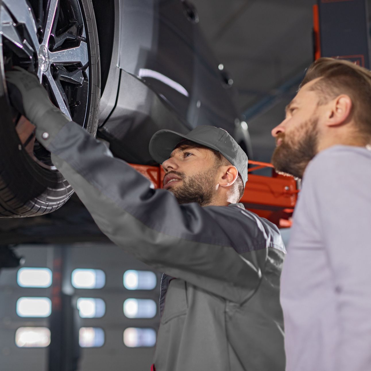 Kfz-Mechatroniker zeigt Kunde etwas am Auto