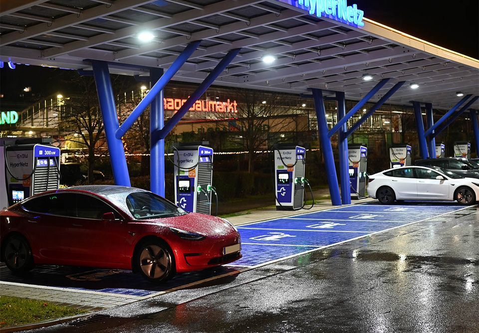 E-Autos nachts an einem Ladepark mit Schnell-Lader, daneben noch freie Ladeplätze