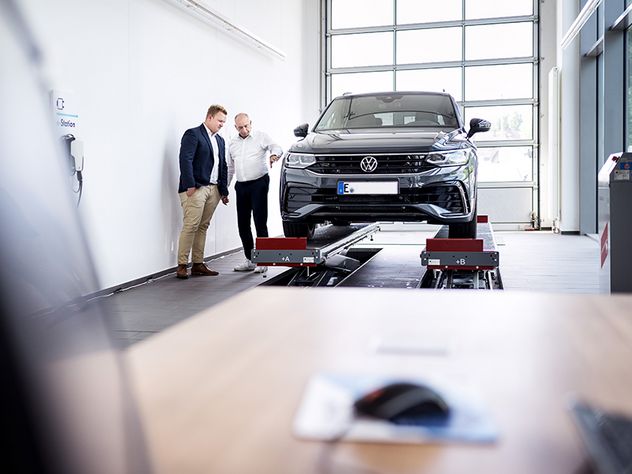 Werkstattkunde und Werkstattmitarbeiter vor einem Kompakt-SUV. DAT Report 2024 Thema des Monats Mai