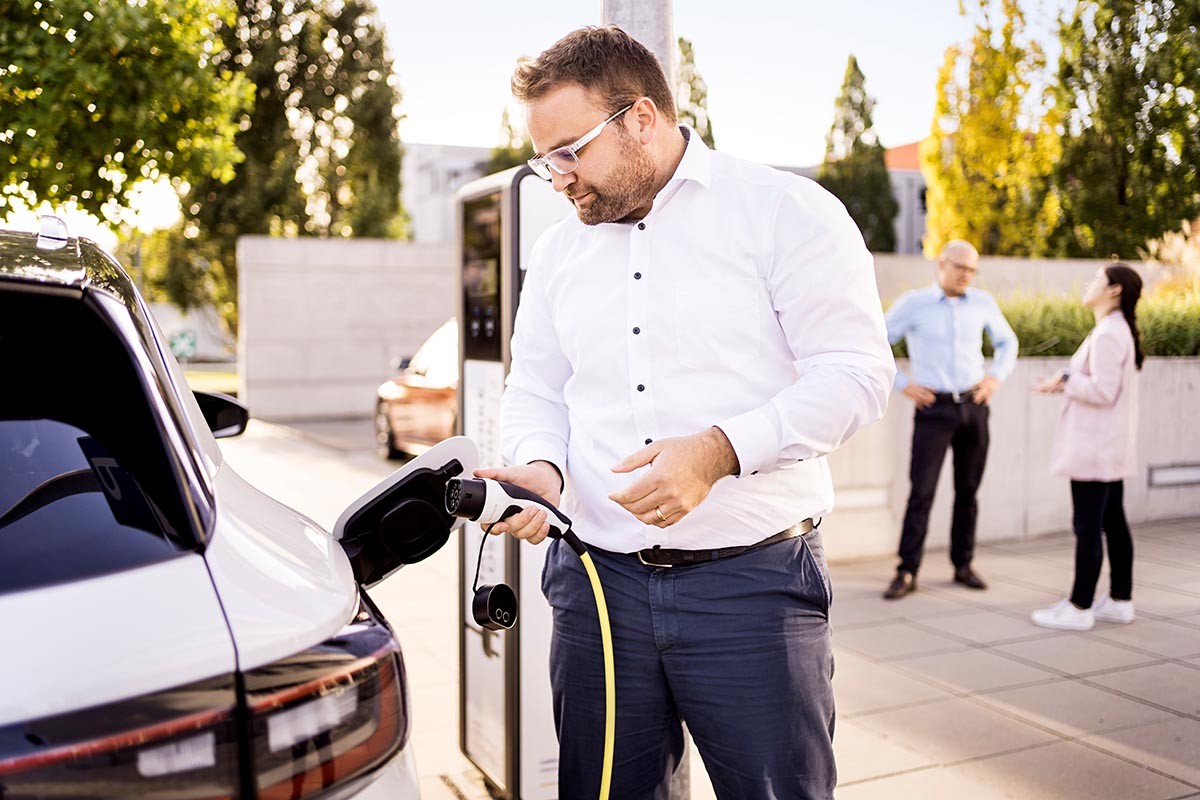 Mann mit AC-Ladekabel an Ladesäule: Welchen Einfluss hat der Akkuzustand auf den Gebrauchtwagenpreis eines E-Autos?