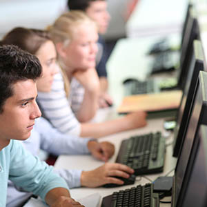Schülerinnen und Schüler einer Berufsschulklasse sitzen vor Desktop-Computern