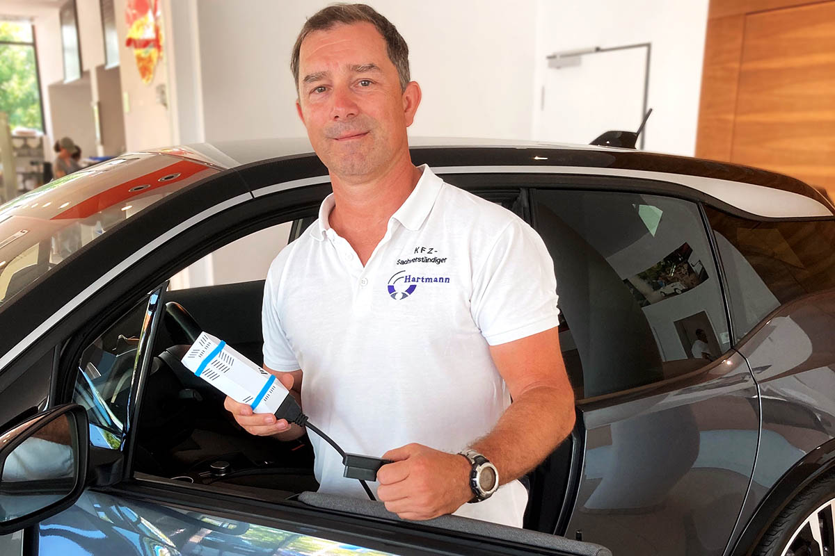 Mike Hartmann, DAT Expert Partner, mit dem Aviloo-Testgerät vor einem BMW i3