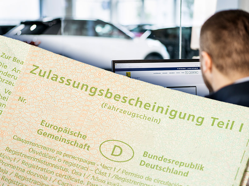 Fahrzeugschein (Zulassungsbescheinigung Teil I) im Vordergrund, im Hintergrund Mitarbeitender eines Autohandelsbetriebs vor dem Computer-Monitor