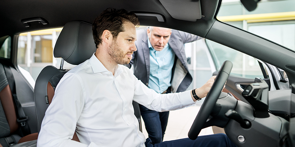 Autoverkäufer und Gebrauchtwagenkäufer schauen sich ein gebrauchtes Fahrzeug von innen an.