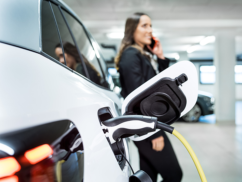 Frau vor Elektroauto. Die DAT ist Anlaufstelle, wenn Endkunden eine Kfz-Werkstatt ihres Vertrauens suchen.