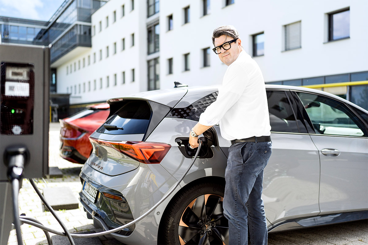 Person steht an einer Ladesäule und lädt sein elektrisches Fahrzeug.