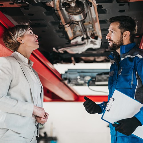 Kundin und Werkstattmitarbeiter unter einem Auto, das sich auf der Hebebühne befindet. DAT-Report Kapitel 4: Werkstatt und Wartung wie war das Verhalten von Autofahrer im Jahr 2022