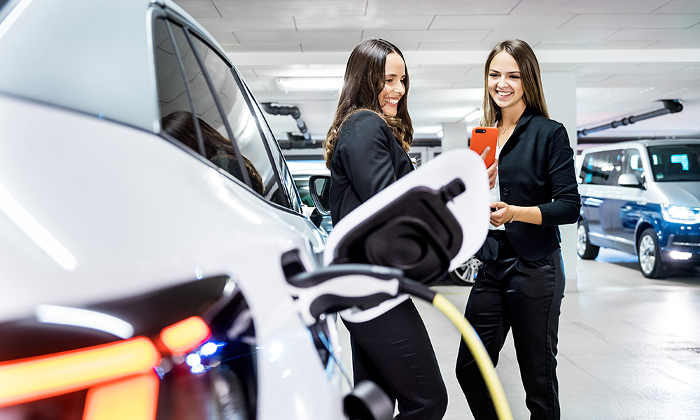 Zwei Frauen vor einem Elektroauto mit Smartphone und Lade-App. 