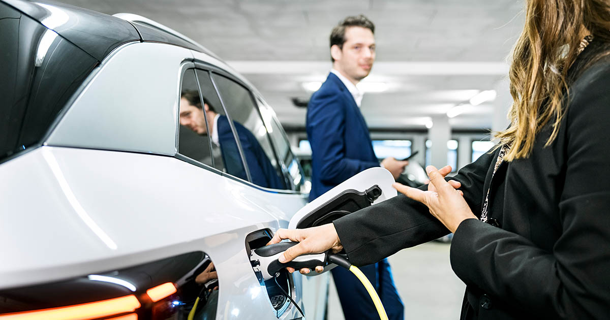 E-Auto wird in Tiefgarage an AC geladen, Mann und Frau unterhalten sich