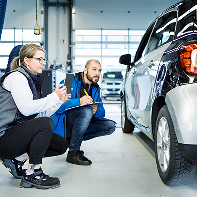 Mitarbeiter aus einem Autohaus begutachtet einen Kotflügel